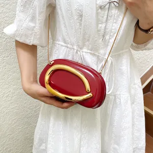 Red structured crossbody bag with gold metal curved handle and chic chain strap for women.