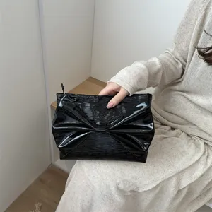 Detailed close-up of a stylish black patent leather evening clutch with a large bow detail.