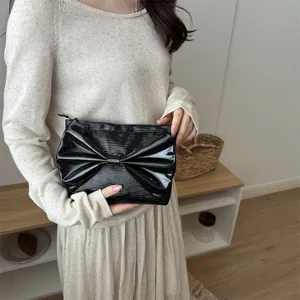 Black patent leather evening clutch bag with chic oversized bow detail close up view.
