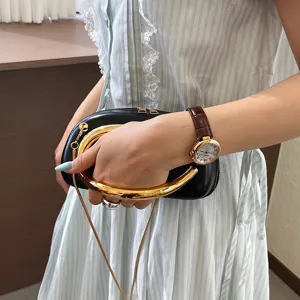 Close-up of a stylish black leather handbag featuring a bold golden curved handle and chain.