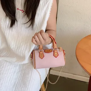 Kids mini pink cylinder shoulder bag with brown handles and elegant gold chain detail.
