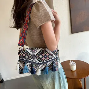 Ethnic style woven crossbody bag detail showing colorful geometric patterns and blue tassels on model.