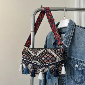 Ethnic woven envelope shoulder bag featuring colorful geometric strap and tassel charms.