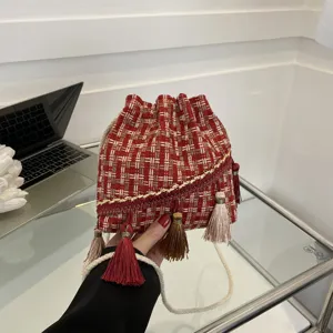 Detailed shot of a stylish woven tweed bucket bag with colorful tassels and shoulder strap.