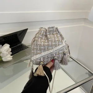 Detailed view of the woven bucket handbag featuring elegant tassels and braided shoulder strap.