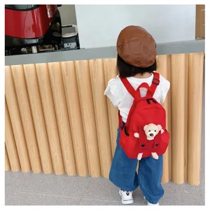 Cute cartoon bear kids backpack detail shot, red canvas schoolbag with plush bear doll.