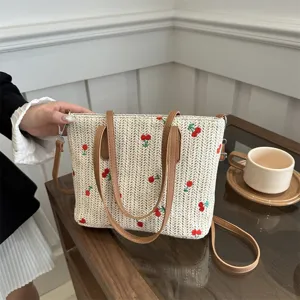 Detailed view of summer straw tote bag with cute red cherry embroidery and brown handles.