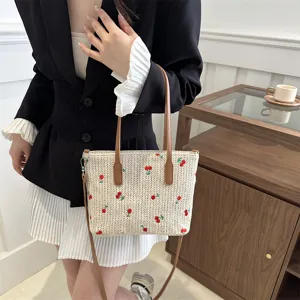 Summer woven tote bag detail, featuring cute cherry embroidery and brown leather shoulder straps.