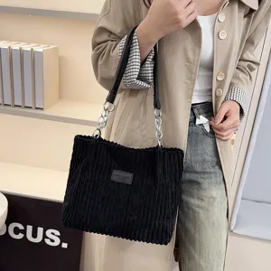 Black corduroy shoulder bag detail with metal chain strap and fabric patch design.