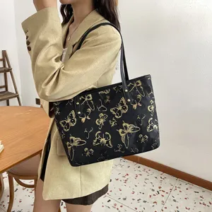 Detail view of women casual black tote bag with gold butterfly embroidery and handles.