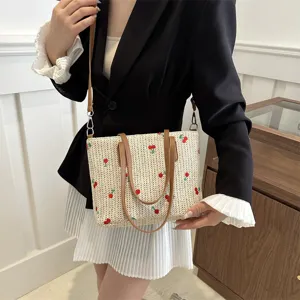 Detailed view of the woven straw shoulder bag featuring cute embroidered cherry patterns.