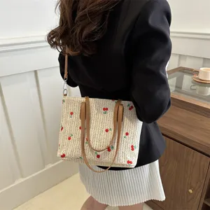 Detailed view of straw woven tote bag with cute red fruit embroidery and brown handles.