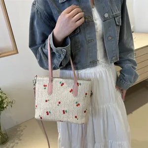 Chic straw tote bag with charming red cherry embroidery, pink leather handles, and spacious design.