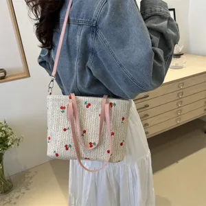 Close-up of the woven straw tote bag featuring cute strawberry embroidery and pink straps.