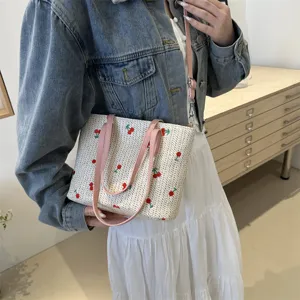 Detailed view of summer woven straw tote bag with cute red cherry embroidery and pink straps.