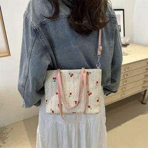 Straw tote bag detail view with cute red cherry embroidery and pink straps for summer travel.