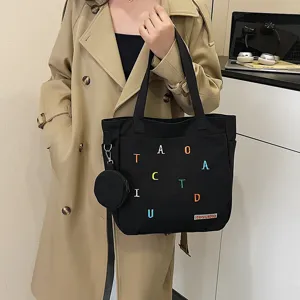 Black canvas tote bag detail, casual shoulder bag with small pouch and colorful letter embroidery.