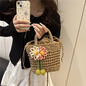 Detailed shot of straw woven bucket bag featuring cute fabric flower pendant and drawstring closure.
