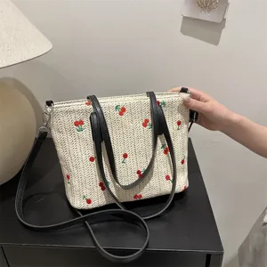 Summer straw woven tote bag detail showing delicate cherry embroidery and stylish leather straps.
