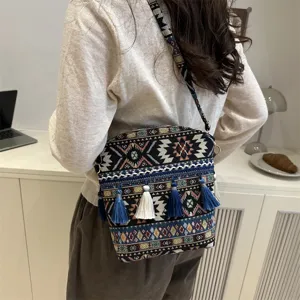 Vue detaillee d'un sac bandouliere ethnique brode de style boheme avec des pompons bleus.