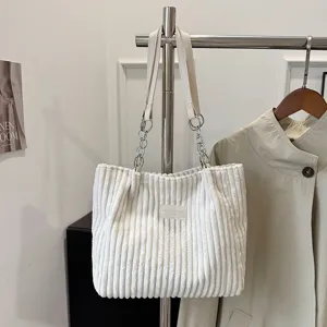 White corduroy shoulder tote bag detail view, showing metal chain strap and fabric label.
