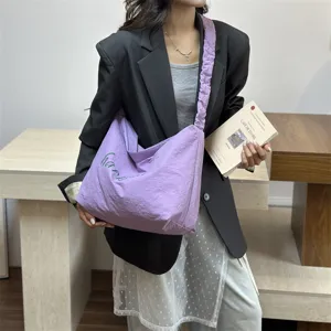 Stylish light purple slouchy shoulder bag with gathered strap and trendy cursive text.
