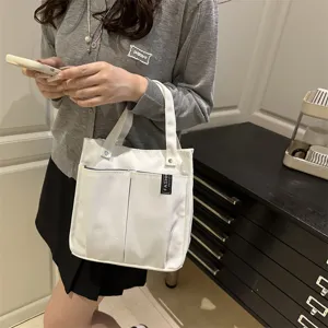 Detailansicht der weißen Segeltuchtasche mit vorderen Taschen und stabilen Henkeln.