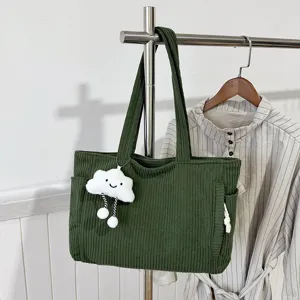 Green corduroy tote bag detail showing fabric texture, cloud plush charm and side pocket.