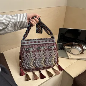 Borsa a tracolla intrecciata in stile etnico con motivi geometrici e dettagli di nappe.