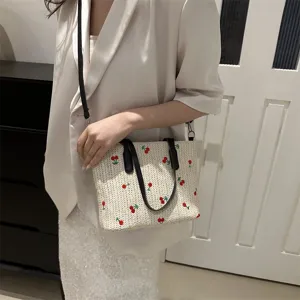 Woven straw detail view showing sweet fruit embroidery, black handles and shoulder strap.