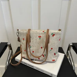 Detailed view of summer woven straw tote bag with brown leather straps and red embroidery.