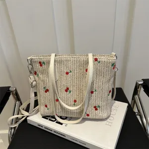 Detail view of woven straw tote bag with cherry embroidery, white PU leather handles and strap.