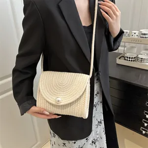Close-up detail shot of the woven straw envelope shoulder bag featuring an elegant pearl clasp.