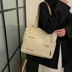 Detail shot of beige canvas tote bag with red embroidery lettering and large capacity storage.
