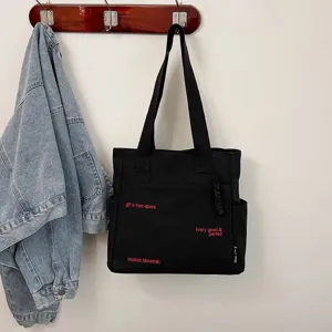 Detail view of the black canvas tote bag hanging on wall hook with red letter prints.