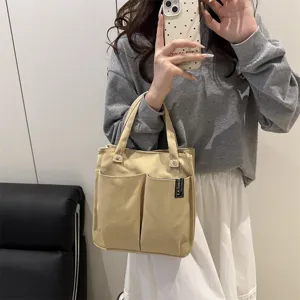 Detailaufnahme der beigen Canvas Tragetasche mit praktischen Vordertaschen und Stofflabel.