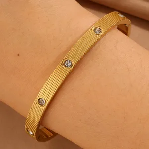 Detailaufnahme eines goldenen Titanstahl-Armreifs mit Streifen und funkelnden Strasssteinen.