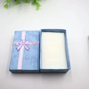 Boite cadeau de bijoux bleue avec ruban noeud violet, emballage elegant pour bagues et colliers.