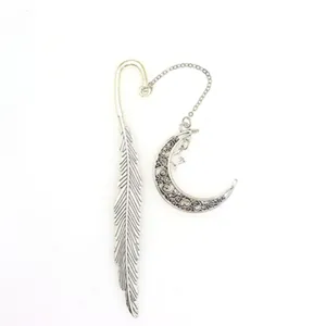Close up of exquisite metal feather bookmark featuring a delicate moon and star pendant.