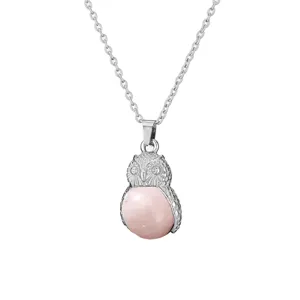 Silver owl pendant necklace close-up, featuring detailed carved wings and a pink gemstone body.
