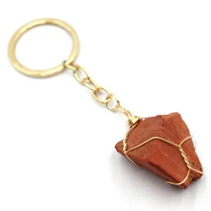 Dettaglio pendente in pietra di cristallo rosso grezzo, primo piano anello portachiavi e catena dorati.