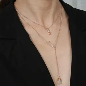 Collier multicouche doré avec pendentif lettre S et goutte en pierre naturelle transparente.