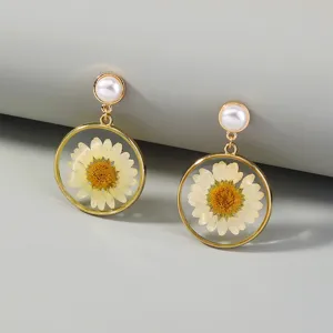 Close-up detail of fashion pressed daisy resin drop earrings with faux pearls and gold frame.