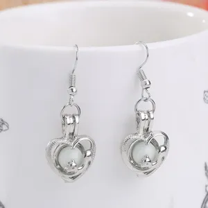 Primer plano de pendientes de plata con corazón hueco, cuenta brillante y detalle de zorro.
