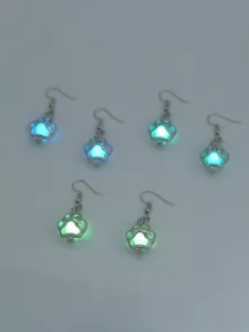 Nahaufnahme von leuchtenden Pfoten Ohrringen, im Dunkeln mit blauem und grünem Licht.