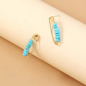 Close-up detail of gold-toned safety pin earrings adorned with turquoise blue beads.