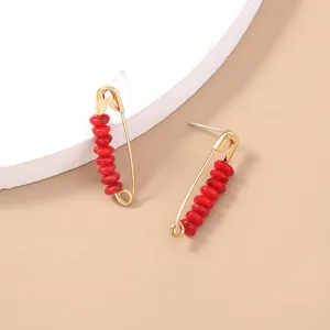 Close-up view of bohemian gold safety pin stud earrings decorated with red disc beads.