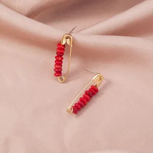Gold safety pin earrings featuring vibrant red beads, perfect for trendy daily style.