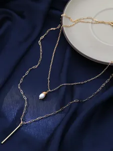 Primo piano della collana a catena dorata multistrato con perla naturale e asta di metallo.