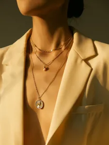 Primo piano di una collana girocollo dorata multistrato con perle e pendente a moneta.
